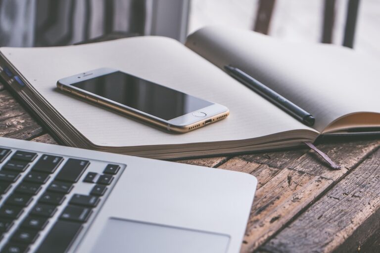 Laptop on a desk with keyboard, phone, and notebook in a clean home office workspace